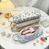 A light blue quilted storage bag for hair dryer and personal items rests on a white table with pink roses.