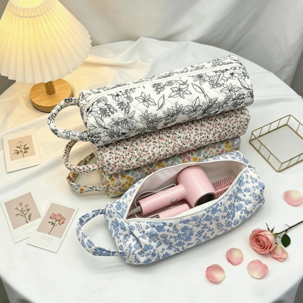 A light blue quilted storage bag for hair dryer and personal items rests on a white table with pink roses.