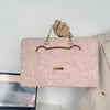 A light pink slim PU laptop sleeve with brown trim and gold hardware being held by a hand.