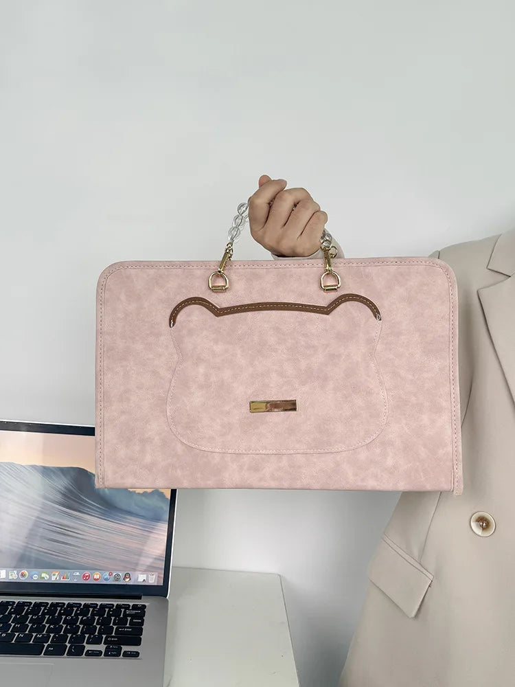 A light pink slim PU laptop sleeve with brown trim and gold hardware being held by a hand.