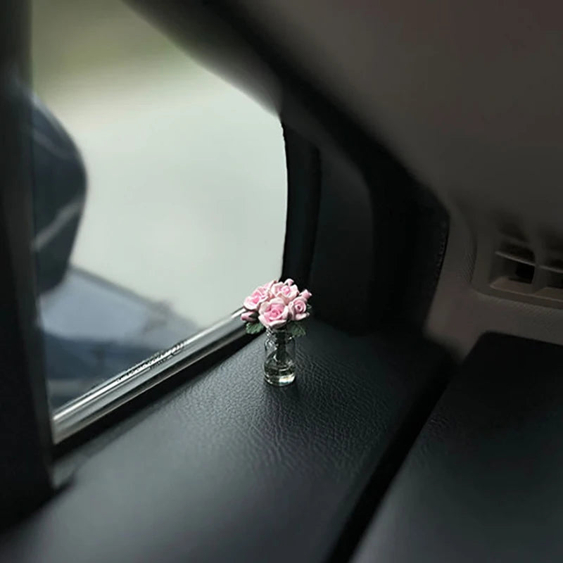 Eine kleine Glasvase mit rosa Rosen auf einer Auto-Innenausstattung.