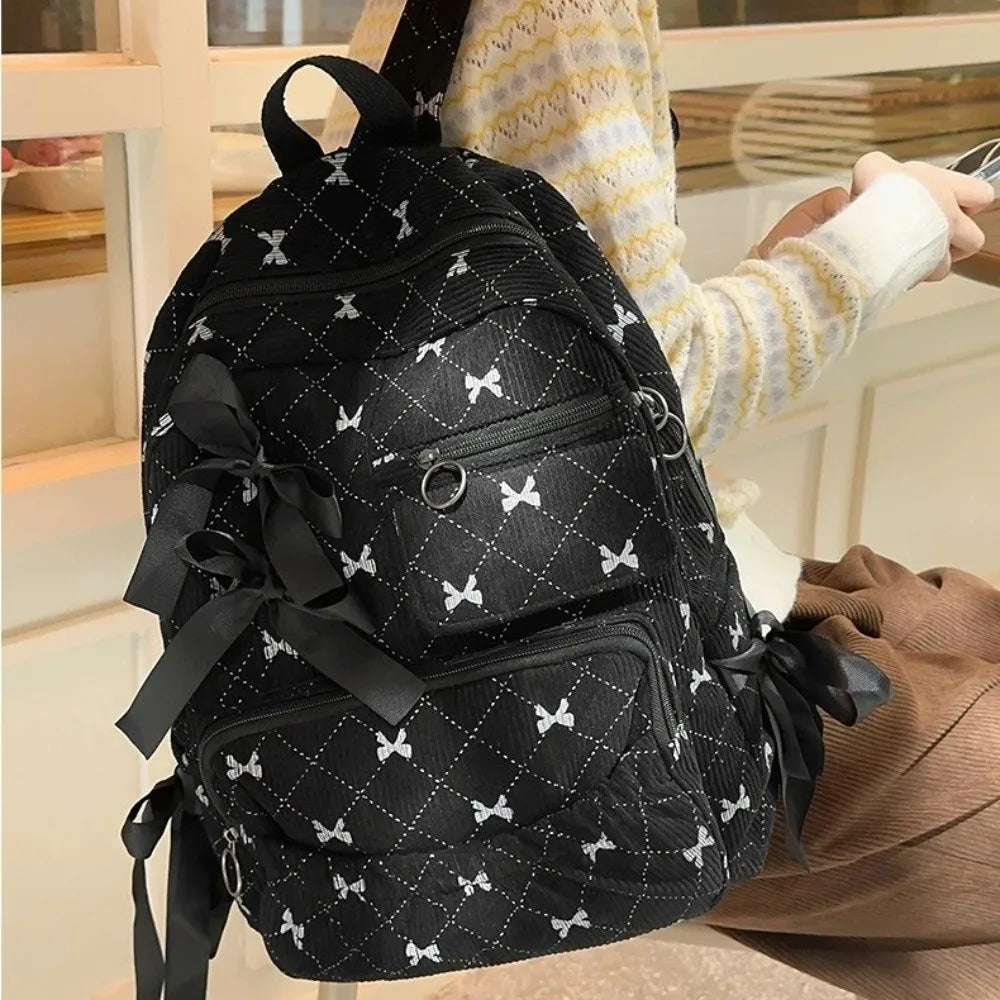 A black corduroy backpack with white bow print details being held by a person.