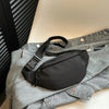 Un sac bandoulière noir en nylon est exposé sur une veste en denim gris.