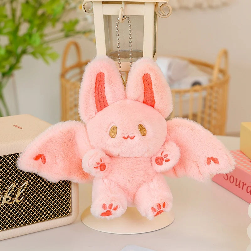 A pink bat bunny plush toy with large ears and soft wings is displayed on a light-colored stand.