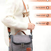 A woman wearing a white sweater is holding a grey insulated reusable lunch bag with a brown strap.