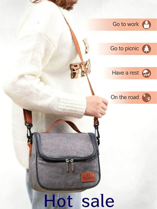 A woman wearing a white sweater is holding a grey insulated reusable lunch bag with a brown strap.