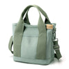 A light sage green canvas crossbody bag with adjustable straps and multiple pockets.