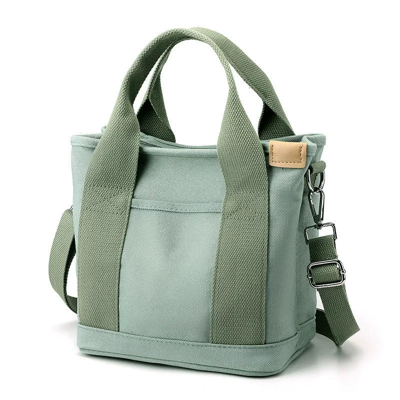 A light sage green canvas crossbody bag with adjustable straps and multiple pockets.