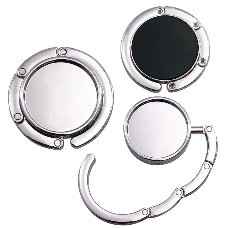 Gancho de bolsa plegable plateado con superficie de espejo circular para organizar artículos.