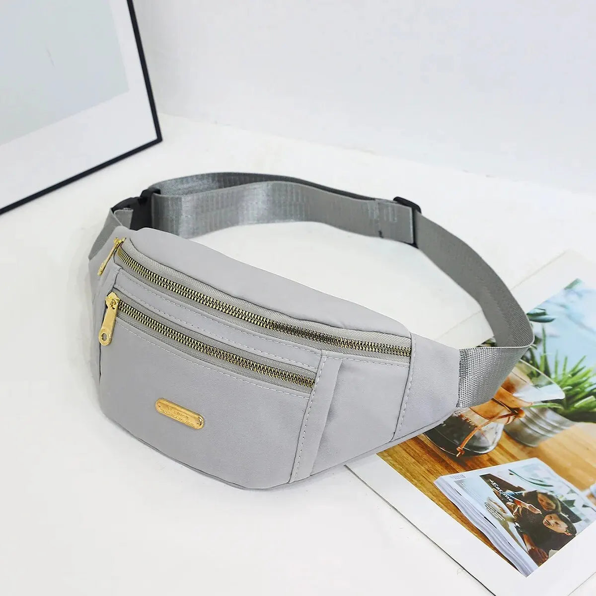 A light gray multi-layer sports waist bag with a zipper and gold accent resting on a white surface.