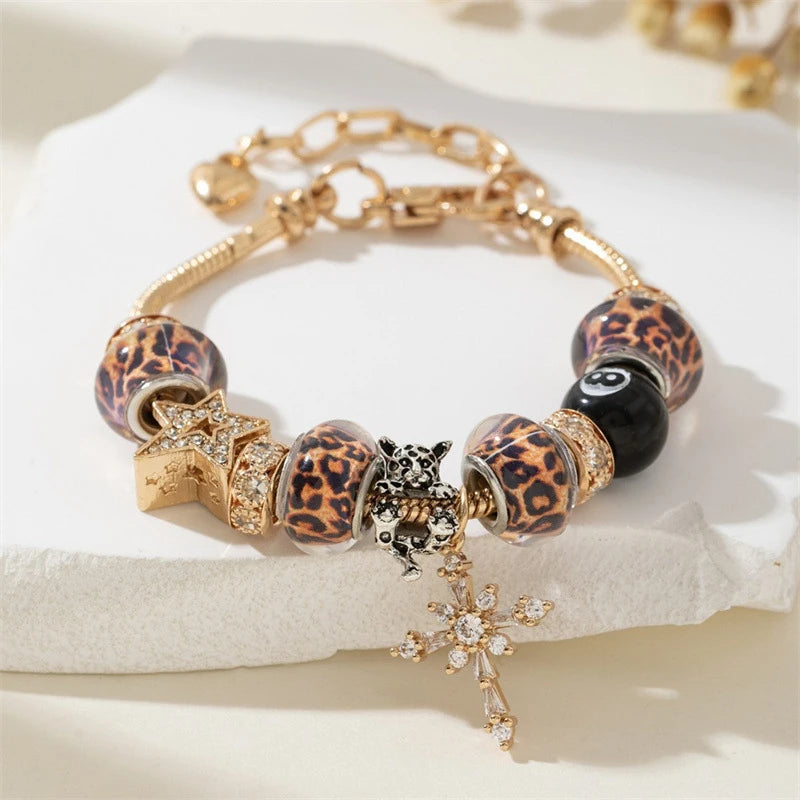 A gold bracelet featuring leopard print beads, black stones, and a silver cross charm.