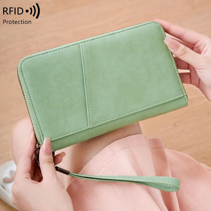 A light green leather RFID blocking travel wallet is shown being held by a person.
