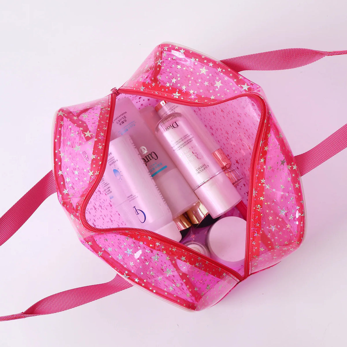 A pink clear waterproof makeup organizer bag containing various cosmetic products and a round compact.