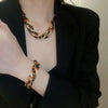 A close-up of a woman wearing a gold leopard print interlocking dangle necklace and bracelet under a black blazer.
