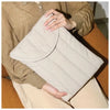 A beige quilted cotton laptop sleeve is held by a person wearing a brown sweater and light pants.