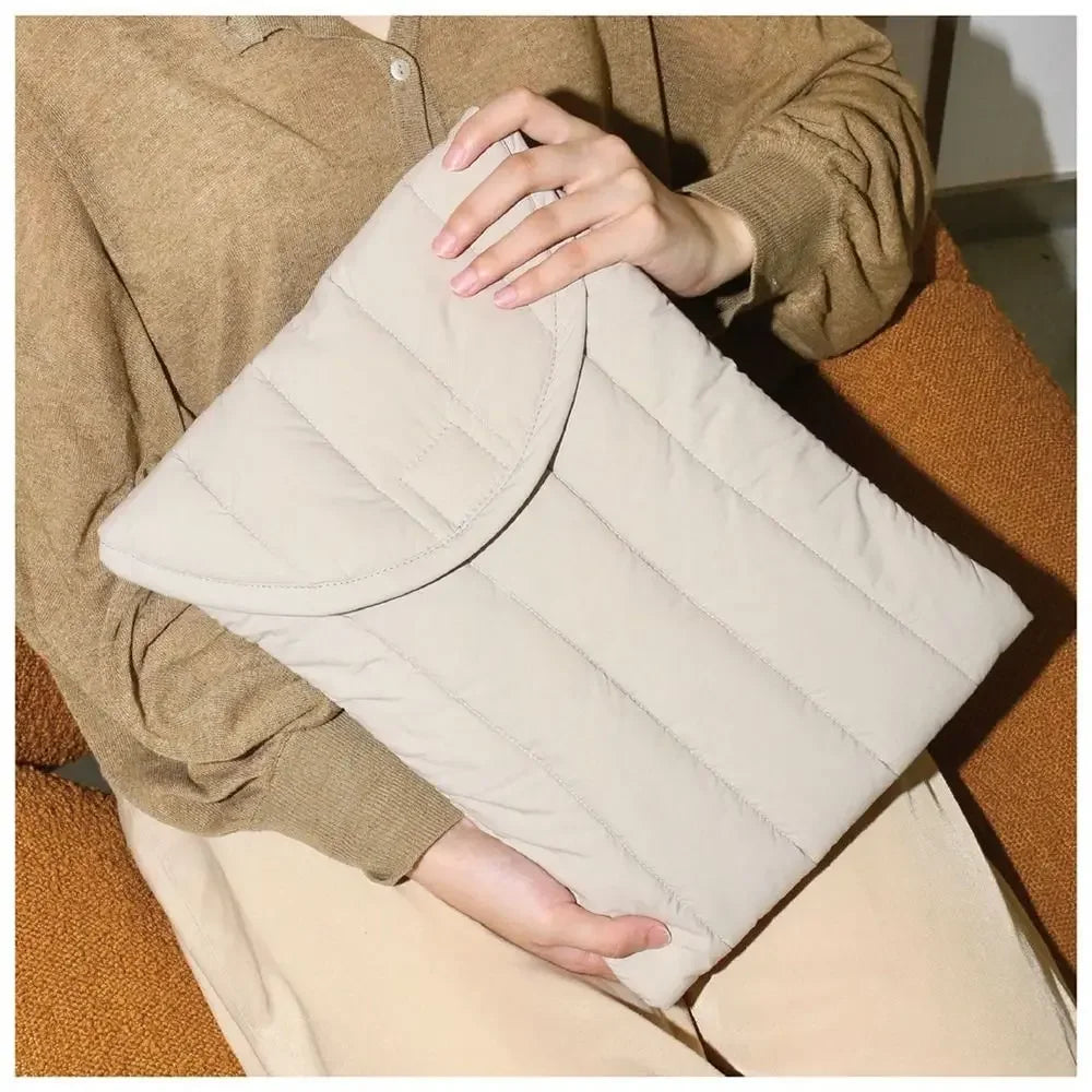 A beige quilted cotton laptop sleeve is held by a person wearing a brown sweater and light pants.
