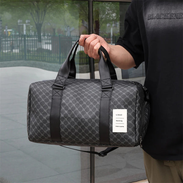 A man holds a black leather-trimmed travel duffle bag with a gray geometric pattern against a glass exterior.