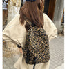 A woman is shown from the back wearing a beige oversized shirt and a leopard print canvas backpack.