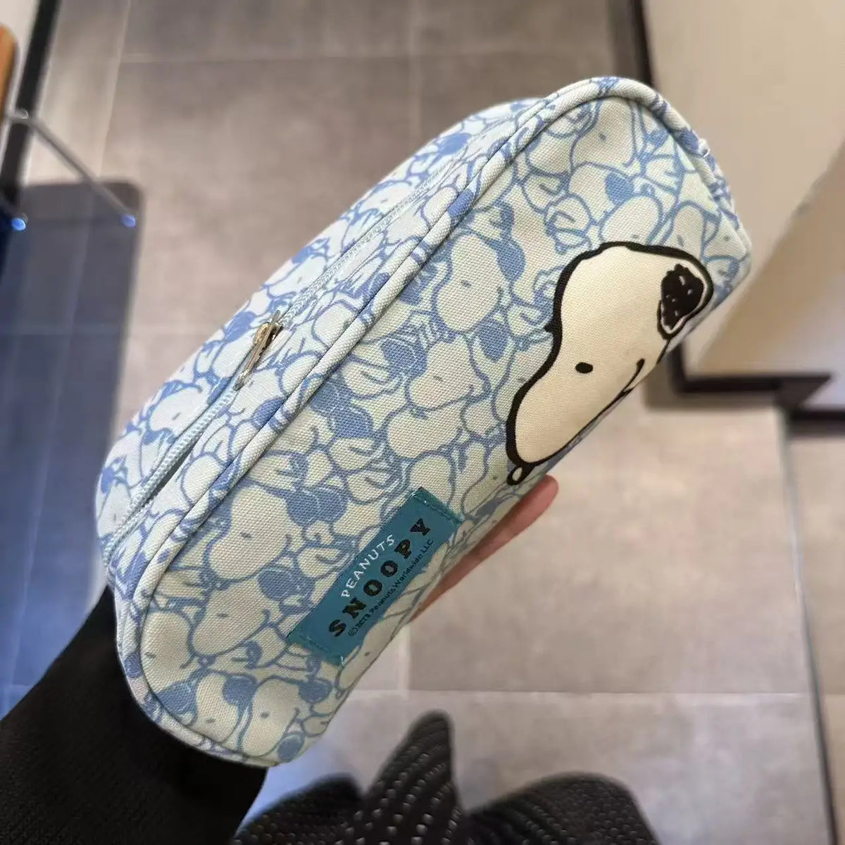 A light blue and white canvas shoulder bag featuring a Snoopy cartoon design, held by a hand.