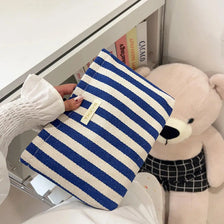 A navy blue and white striped clutch bag is shown resting on a white surface next to a large stuffed animal.