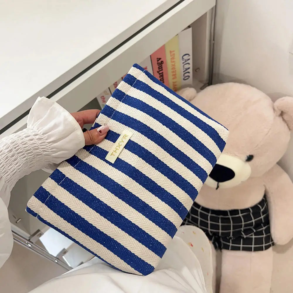 Un bolso de mano a rayas azul marino y blanco reposa sobre una superficie blanca junto a un gran peluche.