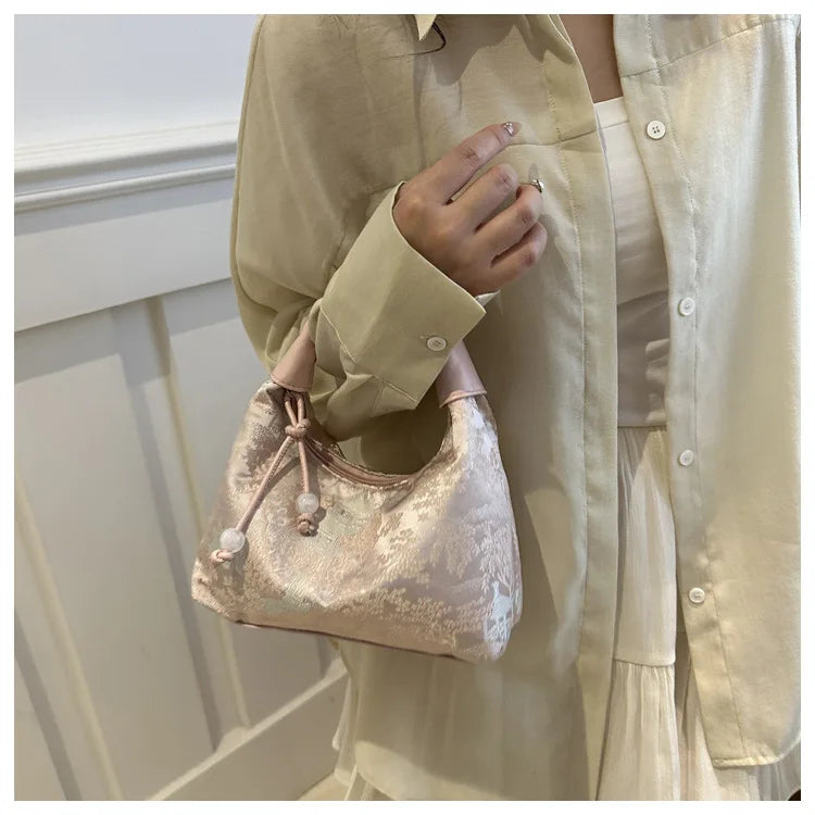 A woman holds a light beige jacket and a pink embroidered crossbody shoulder bag.