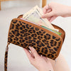 A close-up of a brown leopard print PU leather zipper wallet being held by a hand.