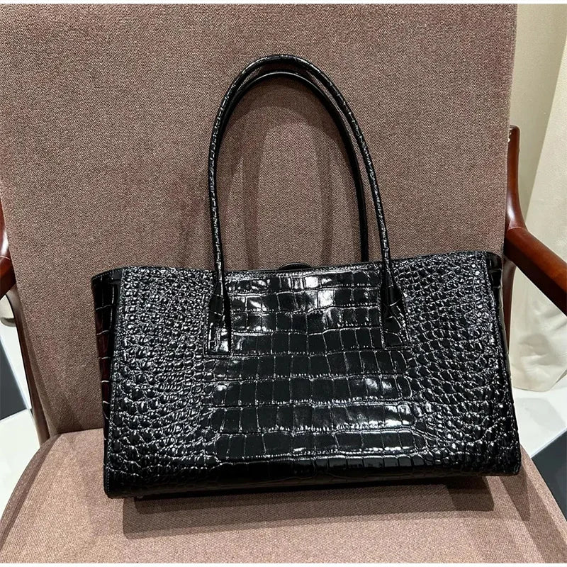 Black crocodile embossed leather tote bag with a black strap resting on a brown chair.