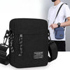 Eine schwarze, kompakte Crossbody-Tasche mit dunkelblauer Akzentfarbe und schwarzem Riemen neben einem weißen T-Shirt.