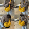 A person wearing a brown sweatshirt holds a yellow canvas crossbody shoulder bag.