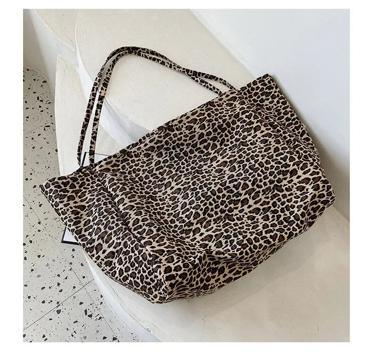 A leopard print canvas crossbody tote bag is displayed on a white surface.