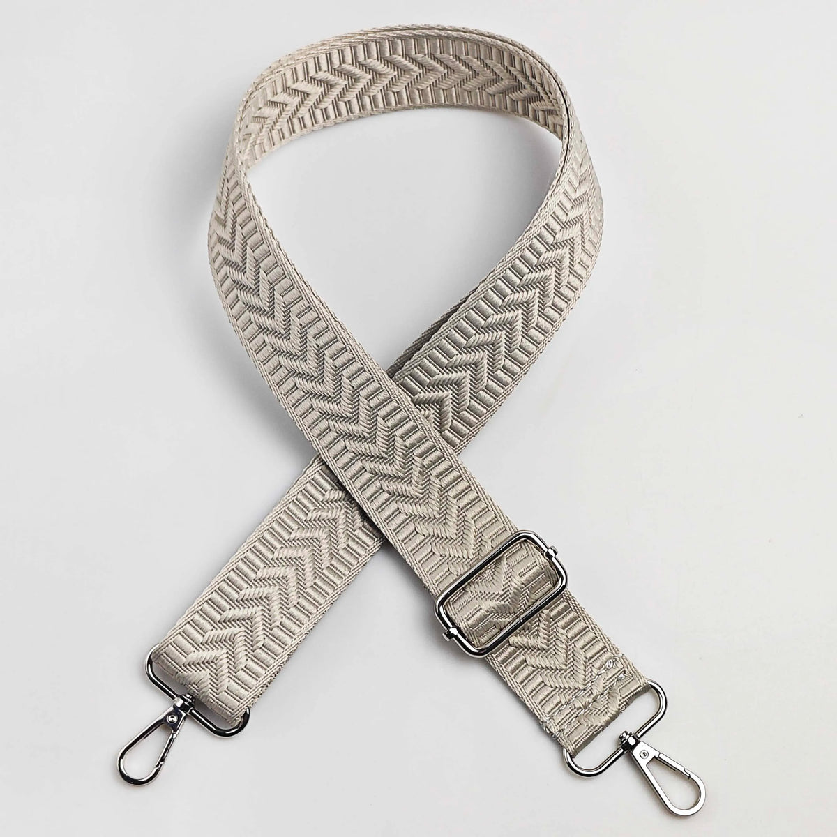 A beige woven strap with an arrow jacquard pattern, shown crossed on a white background.