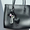 Black PU leather handbag with a white heart keychain featuring a braided black rope.