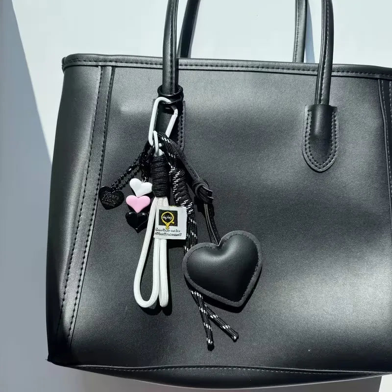 Black PU leather handbag with a white heart keychain featuring a braided black rope.