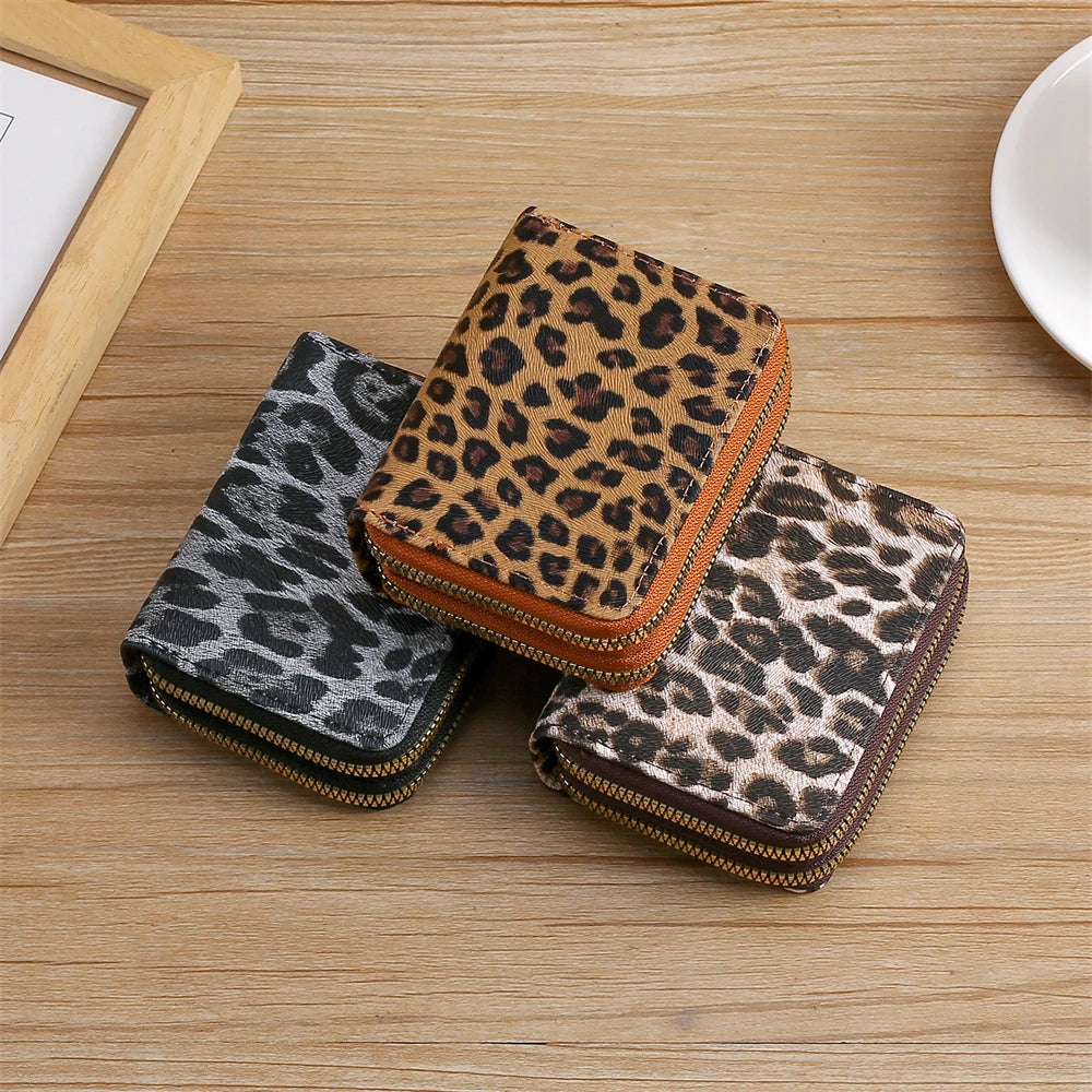A set of three leopard print PU leather compact wallets in various shades of brown and black resting on a wooden surface.