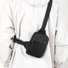 Un hombre sostiene una bolsa cruzada negra impermeable sujetada a una chaqueta blanca con capucha.