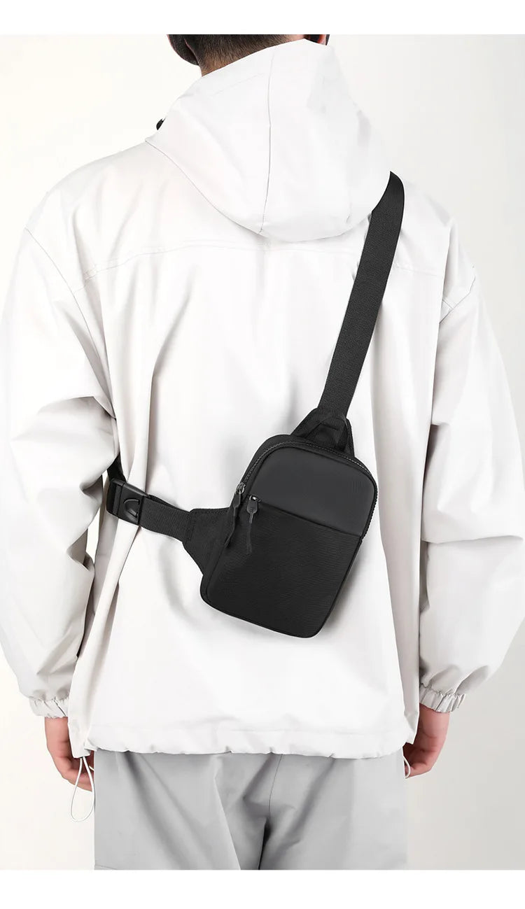 Un hombre sostiene una bolsa cruzada negra impermeable sujetada a una chaqueta blanca con capucha.