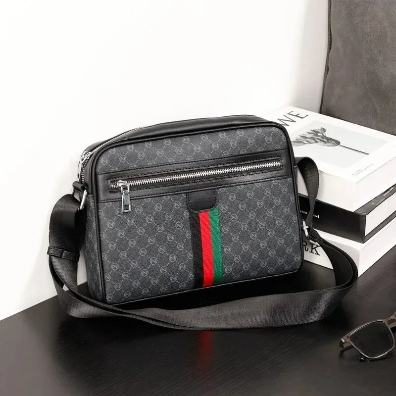 A black men's letter print crossbody sling bag resting on a dark surface next to a white box.