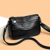 Bolso cruz de cuero negro para mujer con dije plateado y correa negra.