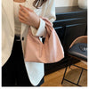 A woman holds a light pink leather minimalist crossbody tote bag against a white blazer and black pants.