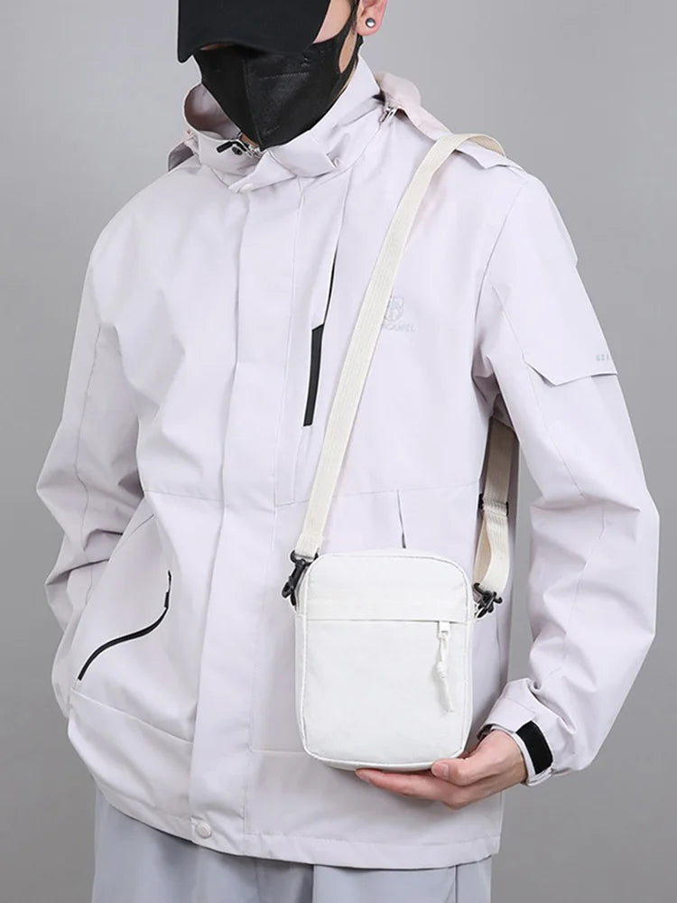Une personne portant une veste blanche et un masque noir tient un sac bandoulière de couleur crème.