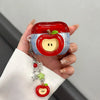 A hand holds a red apple shaped earphone case with a yellow core and green leaf detail.