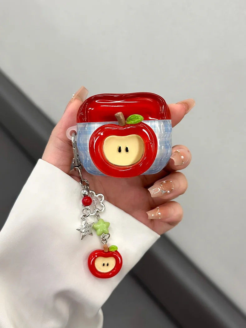 A hand holds a red apple shaped earphone case with a yellow core and green leaf detail.