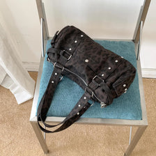 A dark brown leopard print shoulder bag with silver rivets displayed on a metal stand.