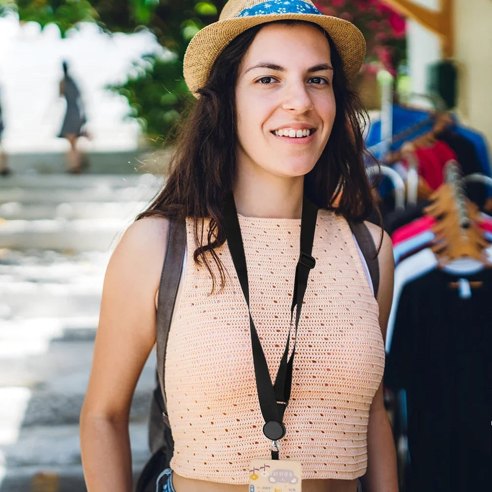 A young woman wearing a light pink top and straw hat is smiling while carrying a black phone lanyard.