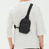 Una bolsa cruzada negra multifuncional llevada sobre una camiseta blanca.