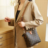 A woman models a tan blazer and beige pants while holding a brown leather bucket bag with a floral pattern.