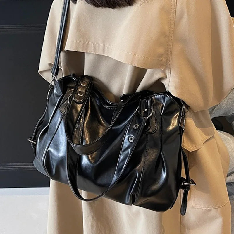 A black leather shoulder bag is shown carried by a person wearing a beige top.