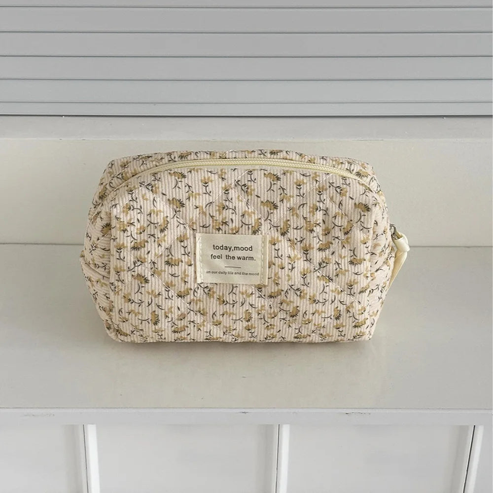 A beige floral print quilted cosmetic bag resting on a white surface.