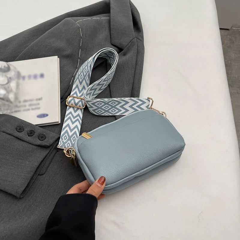 A light blue vegan PU crossbody bag with a patterned strap is shown next to a gray blazer.